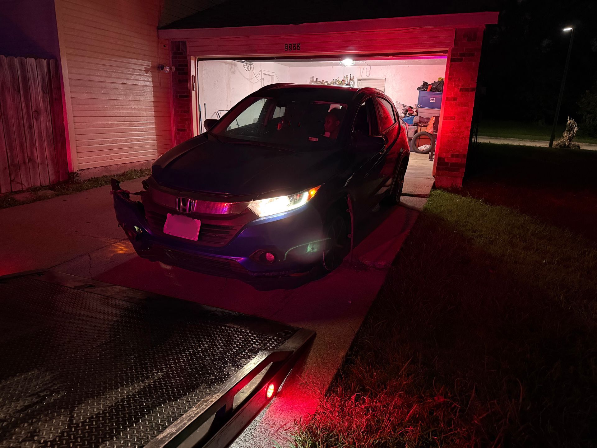 Dark SUV pulled onto a tow truck in front of a garage at night; red lights visible.
