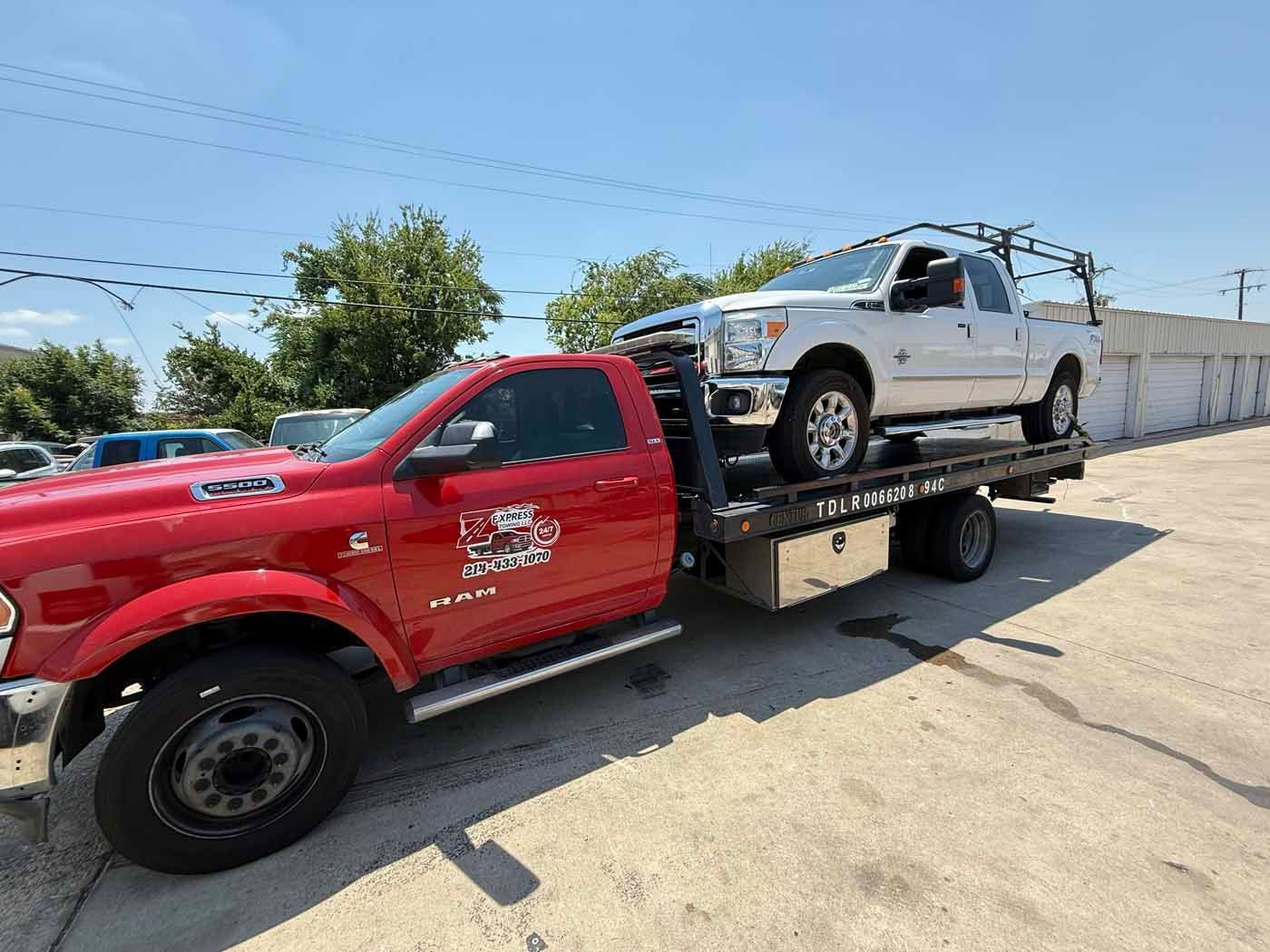 Red tow truck carrying a white pickup truck on a sunny day.