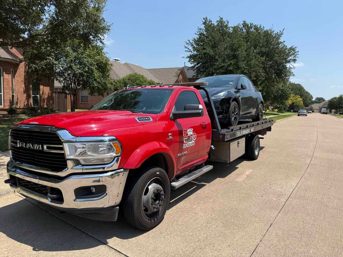 Red tow truck with a dark car on its flatbed parked on a street.